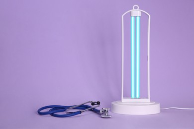 Photo of Ultraviolet lamp and stethoscope on violet background, space for text