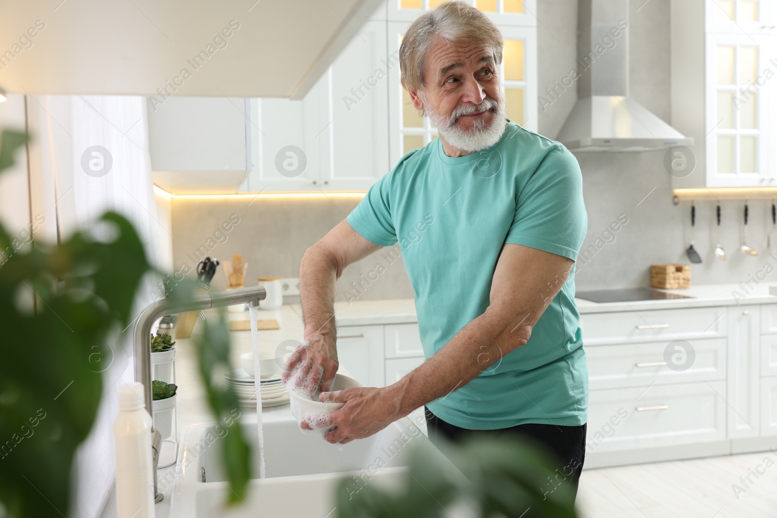 Photo of Senior man washing bowl above sink in kitchen