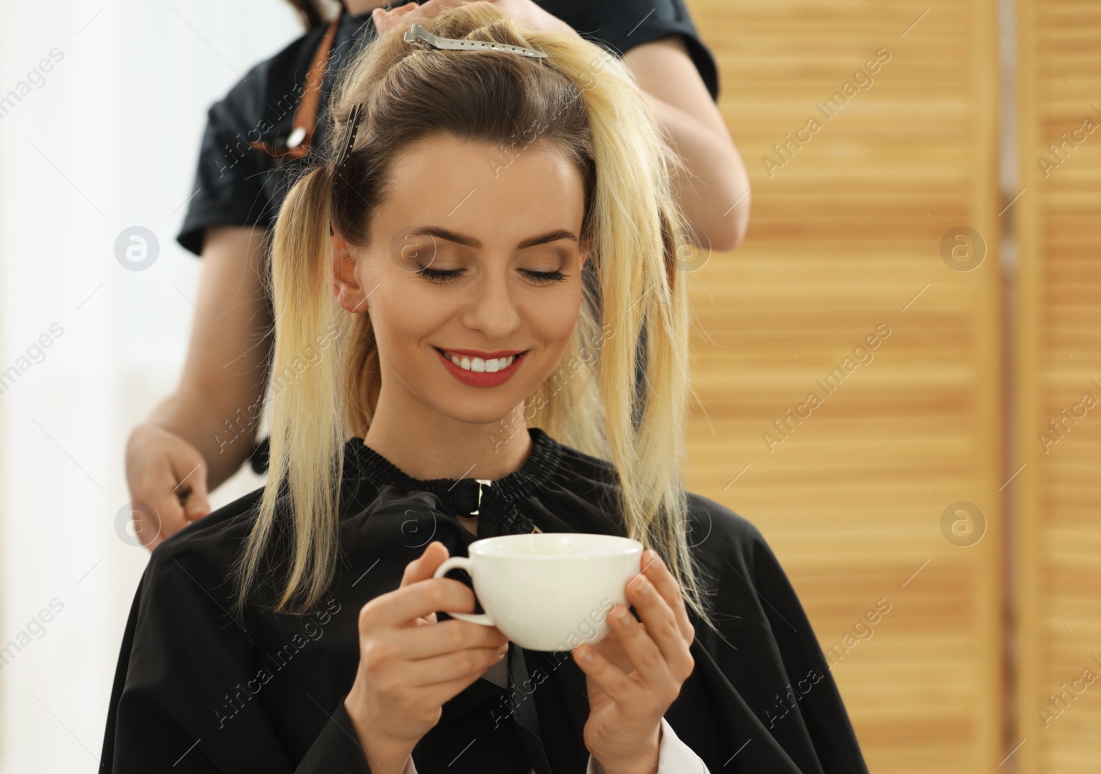 Photo of Hair styling. Professional hairdresser working with woman while she drinking coffee in salon, closeup