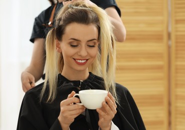 Hair styling. Professional hairdresser working with woman while she drinking coffee in salon, closeup