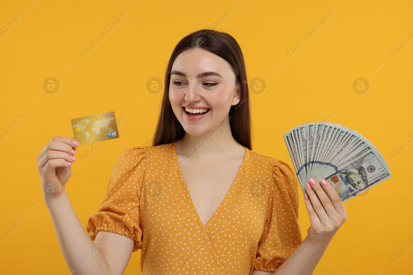 Photo of Happy woman with credit card and dollar banknotes on orange background