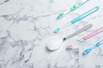 Photo of Flat lay composition with spoon of baking soda, toothbrushes and space for text on marble background