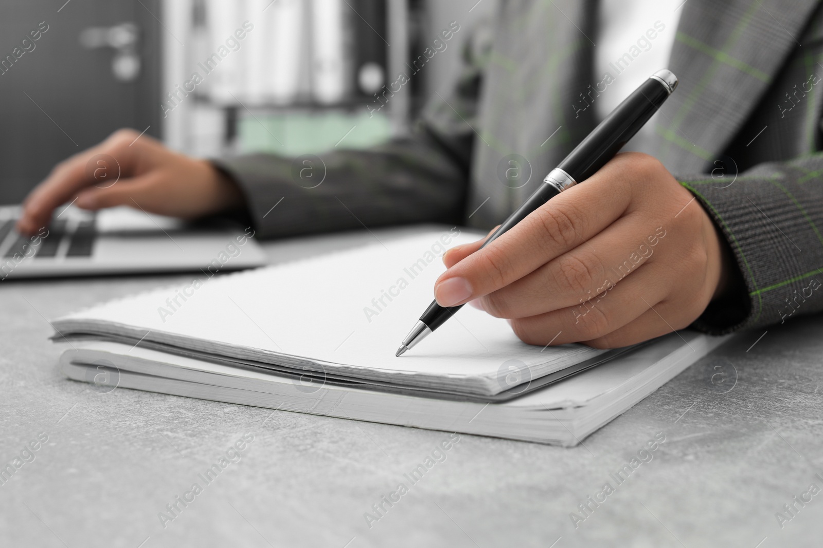 Photo of Woman working with laptop and writing in notebook at table indoors, closeup