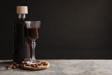 Photo of Bottle of coffee liqueur, shot glass and beans on light grey table, space for text