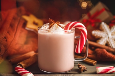 Photo of Glass cup of tasty cocoa with marshmallows and Christmas candy cane on wooden table