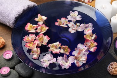 Photo of Bowl of water with flowers, stones and candles on wooden table. Spa treatment