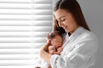 Mother holding her cute newborn baby indoors. Space for text