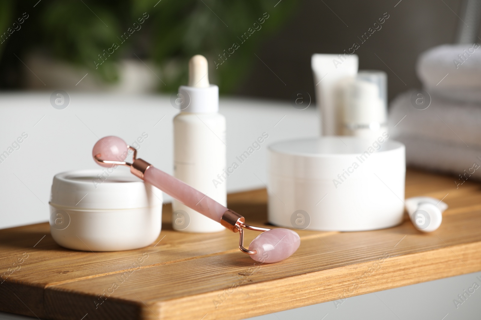 Photo of Bath tray with natural face roller and cosmetic products on tub, closeup