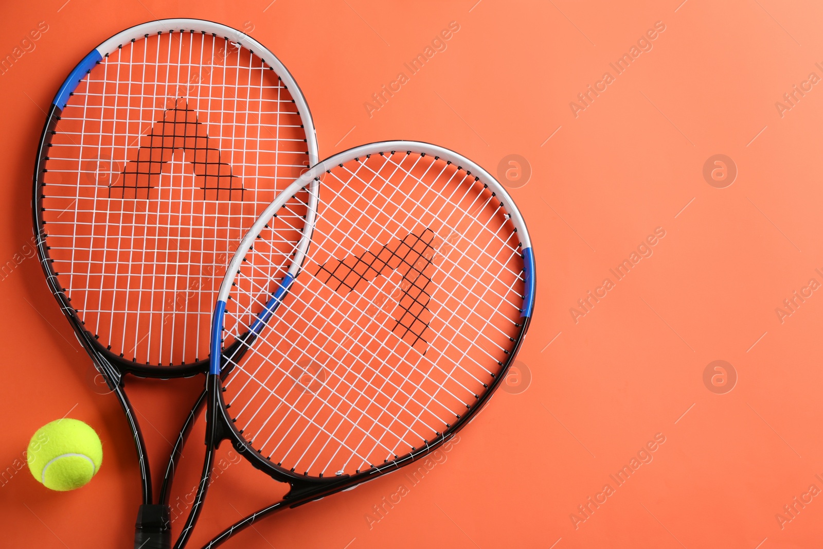 Photo of Tennis rackets and ball on orange background, flat lay. Space for text