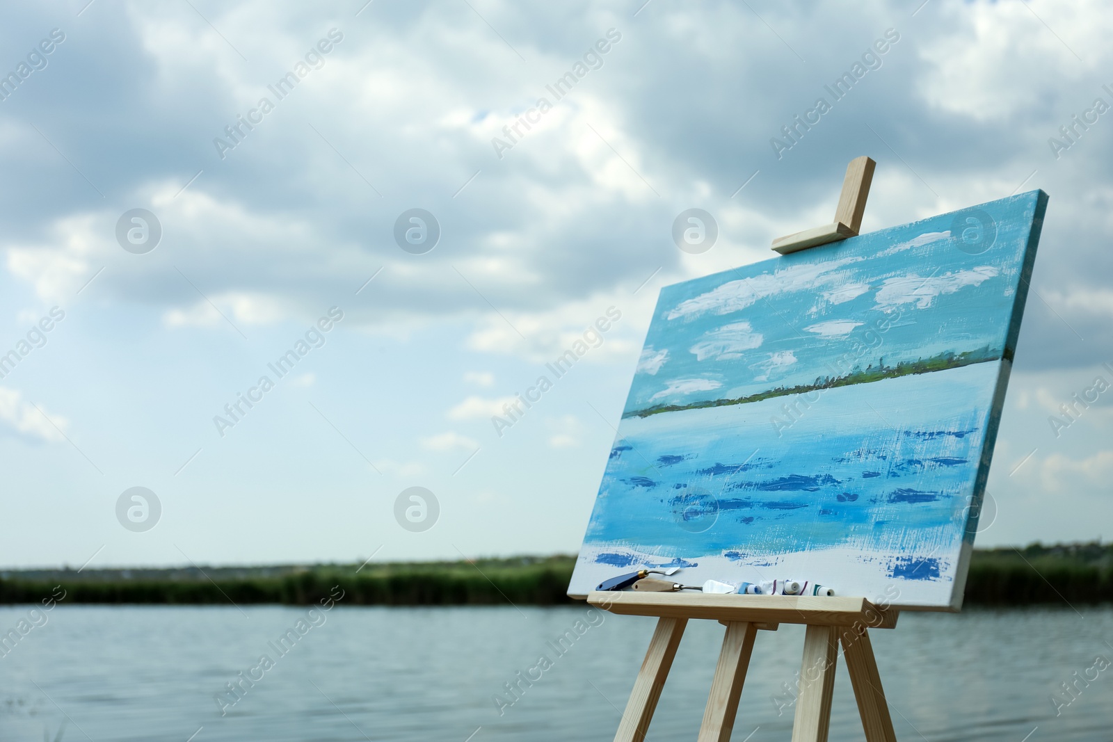 Photo of Wooden easel with unfinished painting near lake