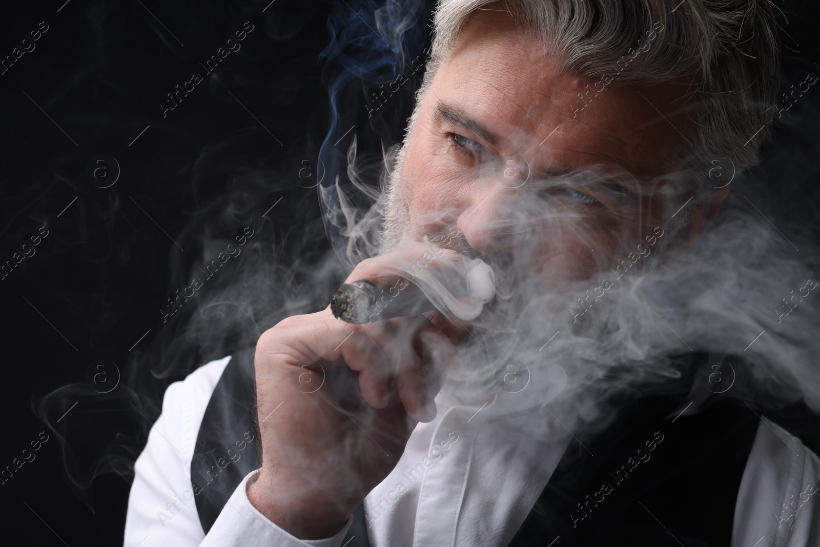 Photo of Bearded man smoking cigar against black background