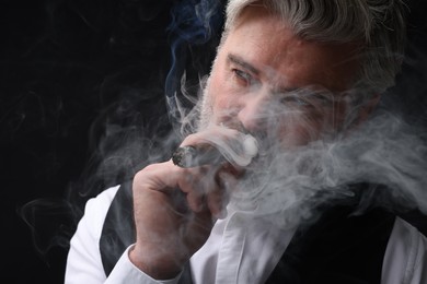 Photo of Bearded man smoking cigar against black background