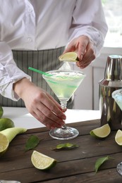 Photo of Bartender squeezing lime juice into glass with delicious Margarita cocktail at wooden table, closeup