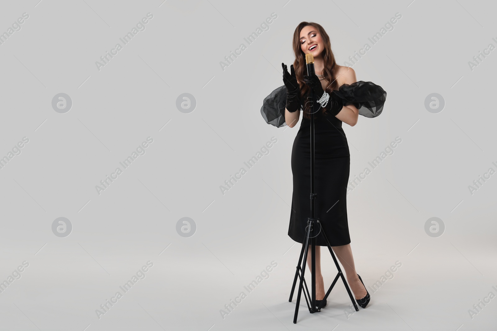 Photo of Beautiful young woman in stylish dress with microphone singing on light grey background, space for text