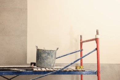 Photo of Different tools on tower tour near white wall with adhesive mix and tiles indoors