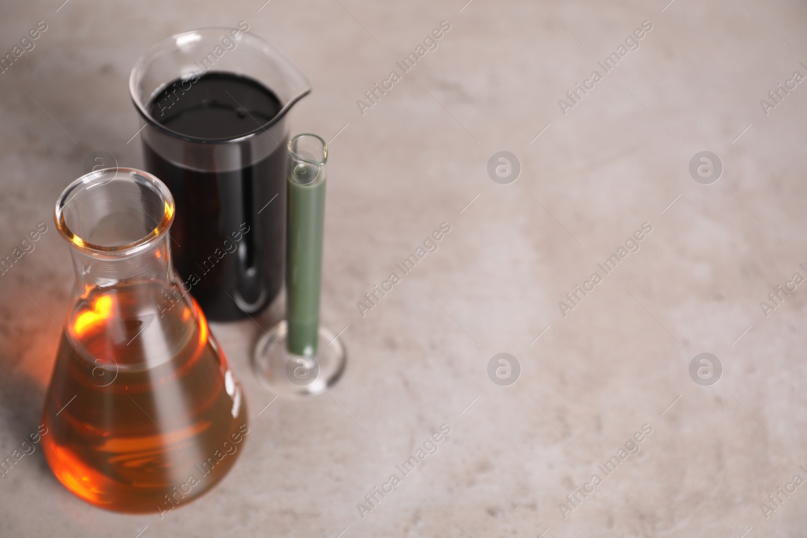 Photo of Test tube, beaker and flask with different types of oil on grey table, closeup. Space for text