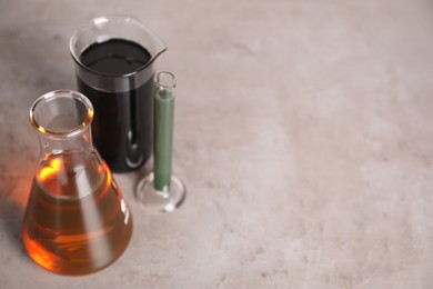 Test tube, beaker and flask with different types of oil on grey table, closeup. Space for text