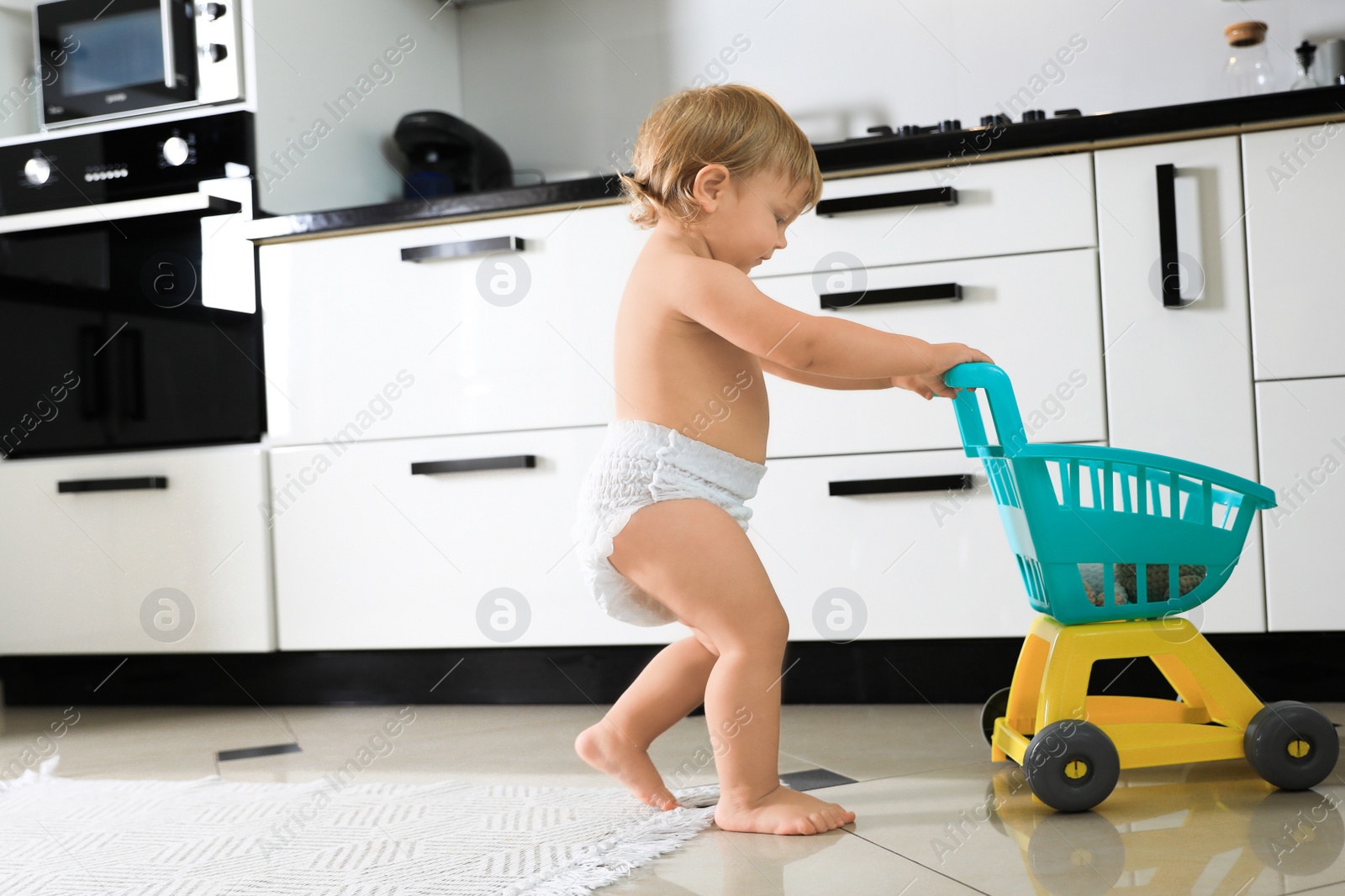 Photo of Cute baby with toy walker in kitchen. Learning to walk