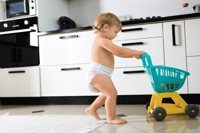 Cute baby with toy walker in kitchen. Learning to walk