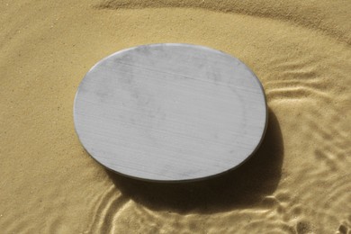 Photo of Stylish presentation for product. Stone podium in water on sand, top view