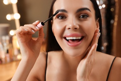 Beautiful young woman applying mascara in dressing room, closeup