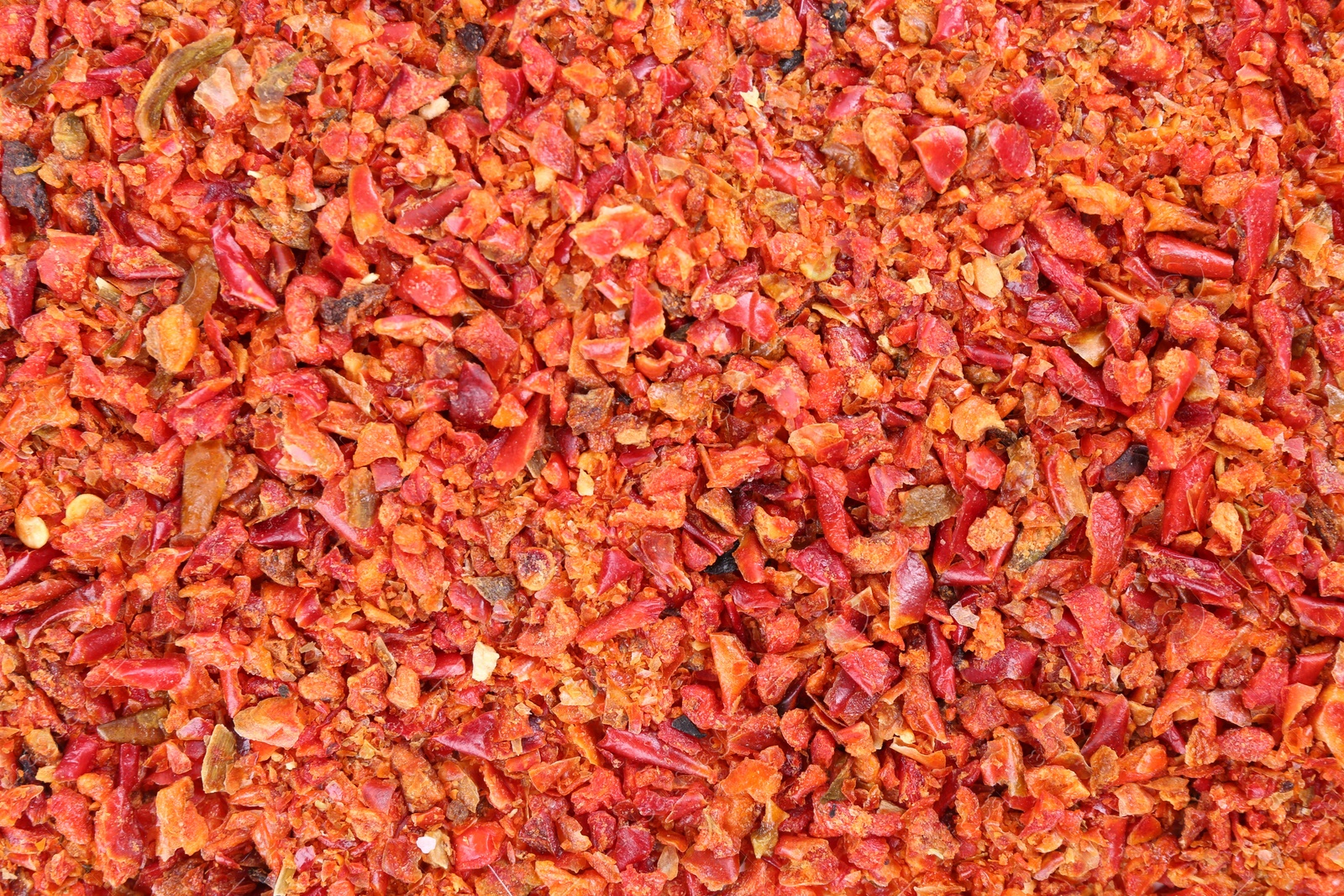 Photo of Aromatic spice. Red chili pepper flakes as background, top view