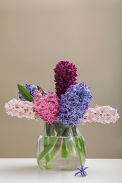 Beautiful hyacinths in glass vase on table against color background, space for text. Spring flowers