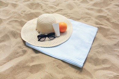 Beach accessories and orange on sand, above view