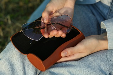 Photo of Woman holding sunglasses in brown leather case outdoors on sunny day, closeup
