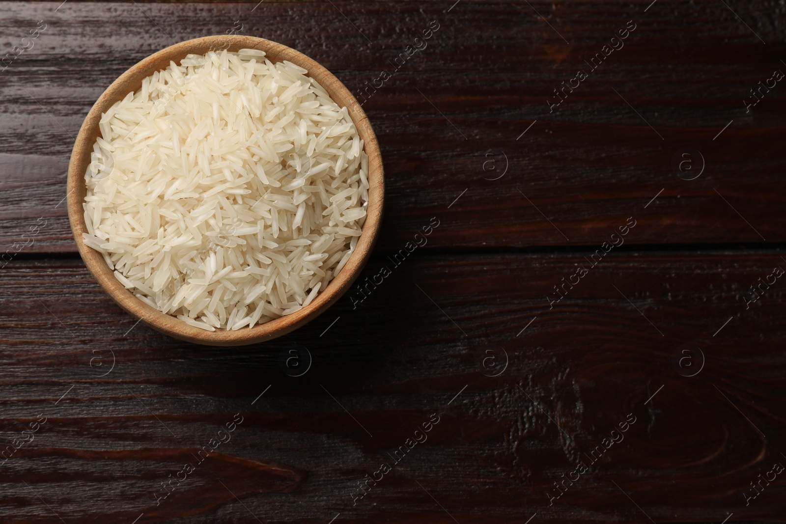 Photo of Raw basmati rice in bowl on wooden table, top view. Space for text