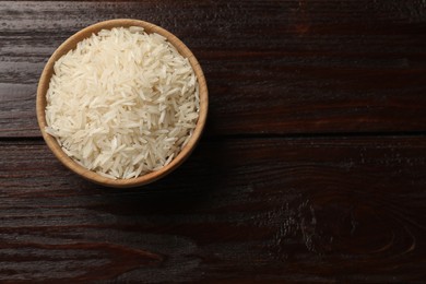 Photo of Raw basmati rice in bowl on wooden table, top view. Space for text