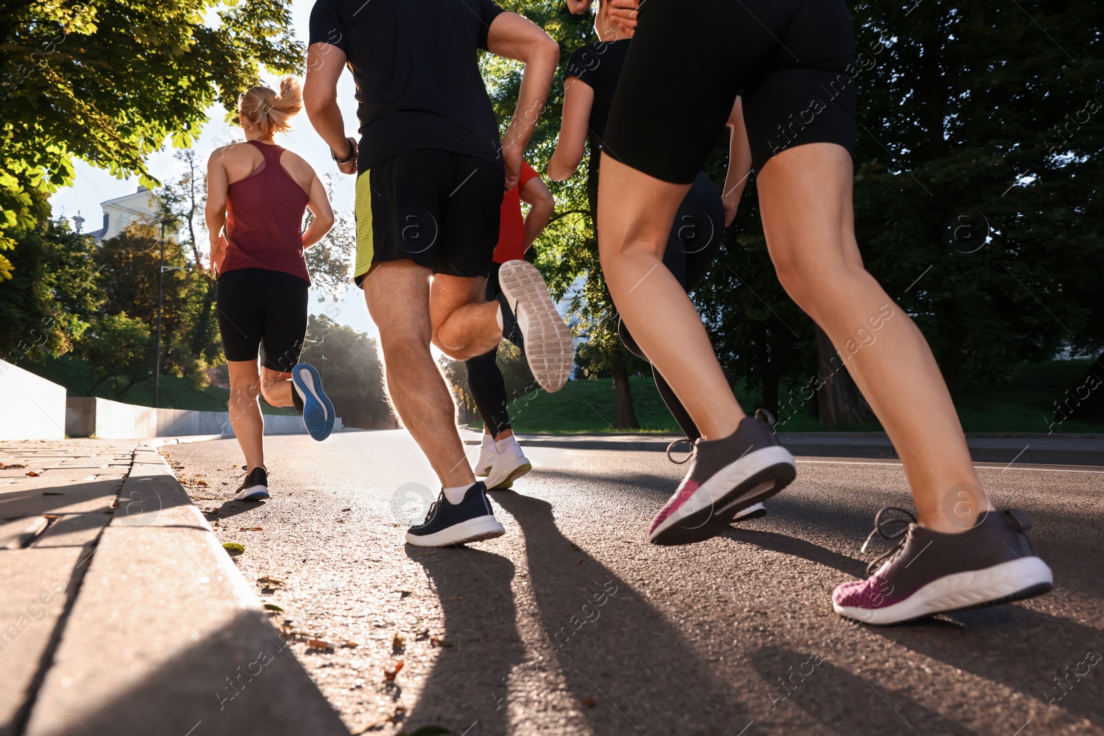 Photo of Group of people running outdoors on sunny day, back view