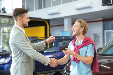 Salesman shaking hands with customer while giving car key in auto dealership