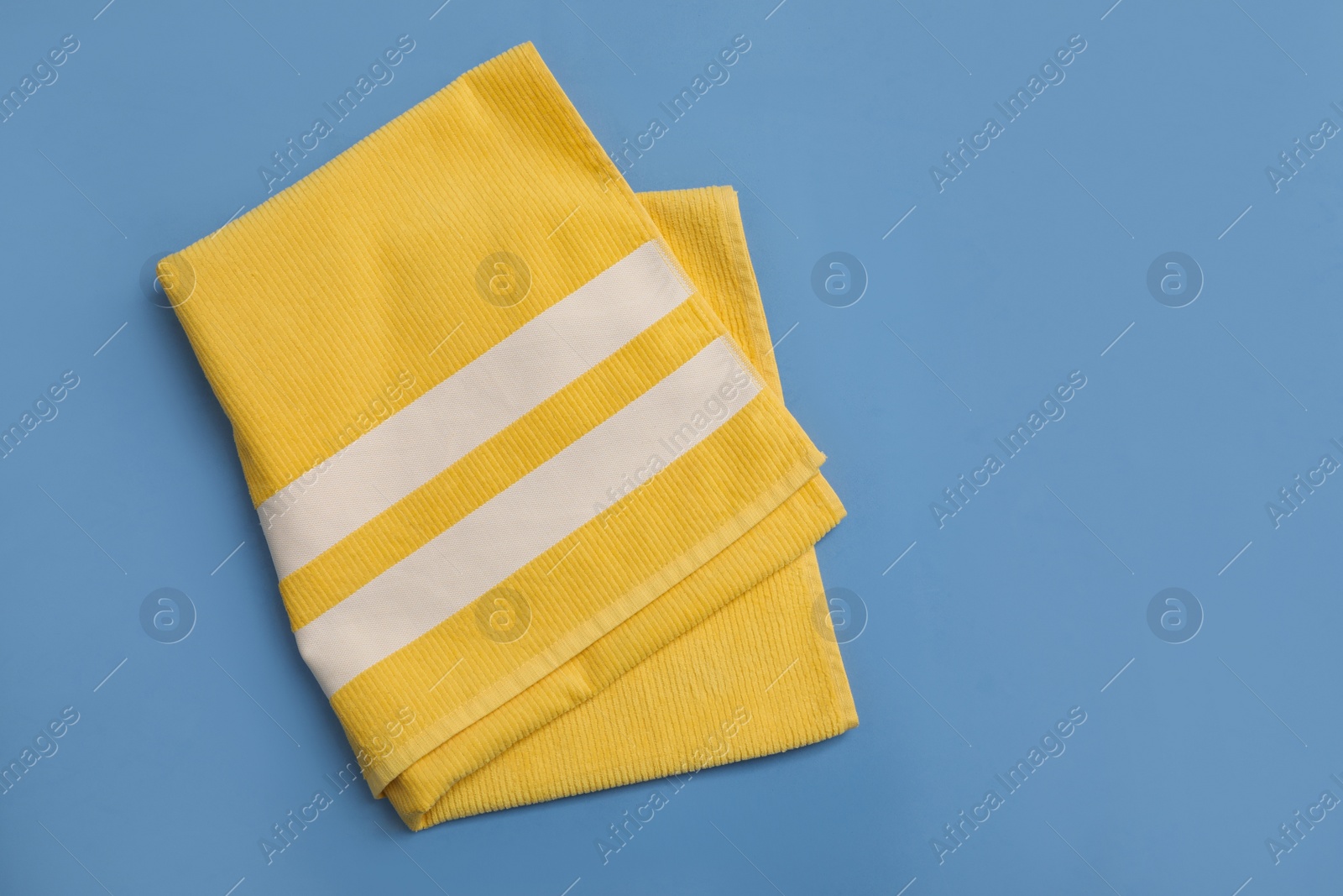 Photo of Folded yellow beach towel on blue background, top view. Space for text