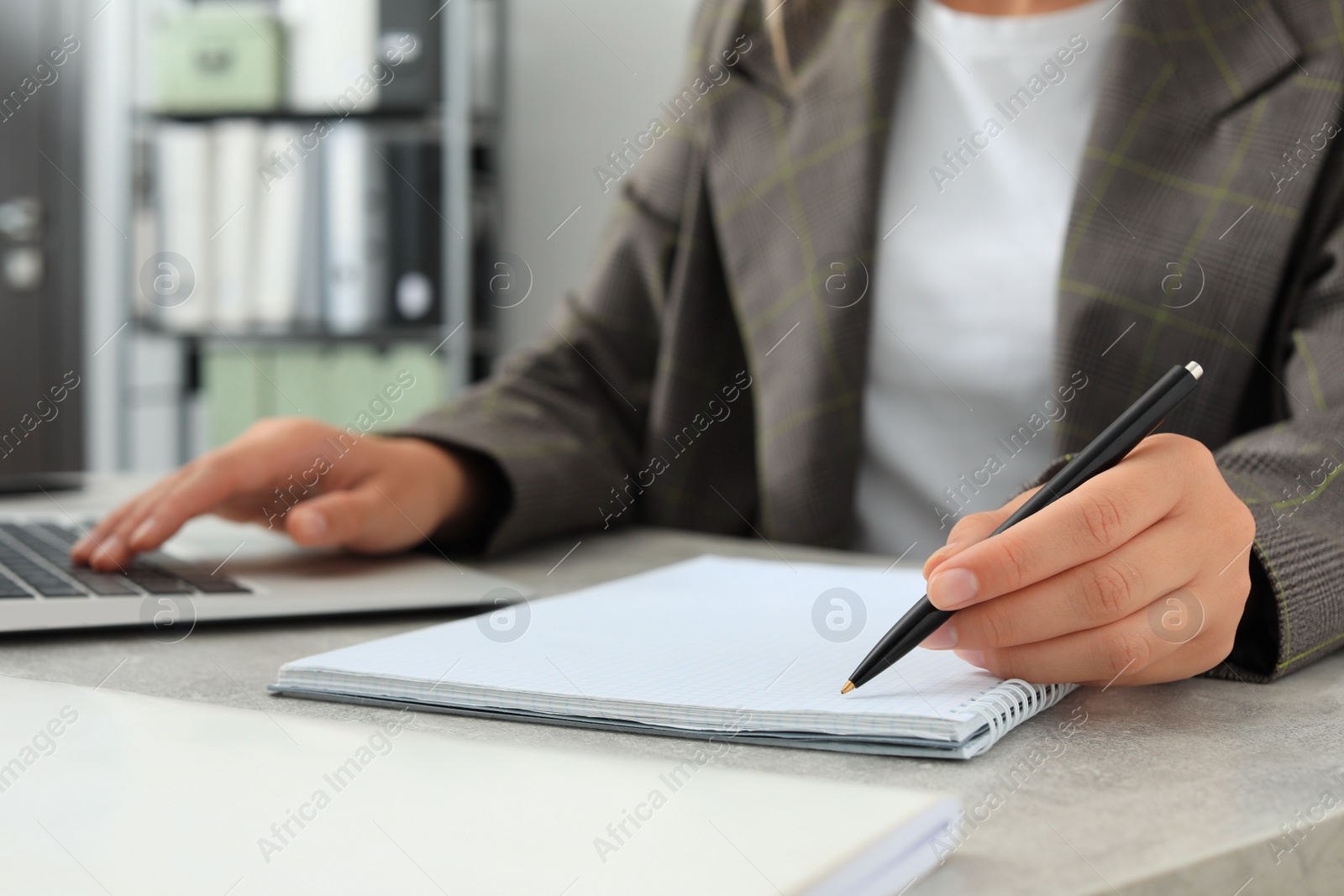 Photo of Woman working with laptop and writing in notebook at table indoors, closeup