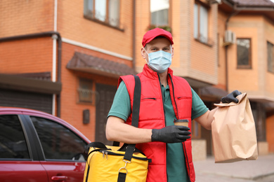 Photo of Courier in protective mask and gloves with orders near car outdoors. Food delivery service during coronavirus quarantine