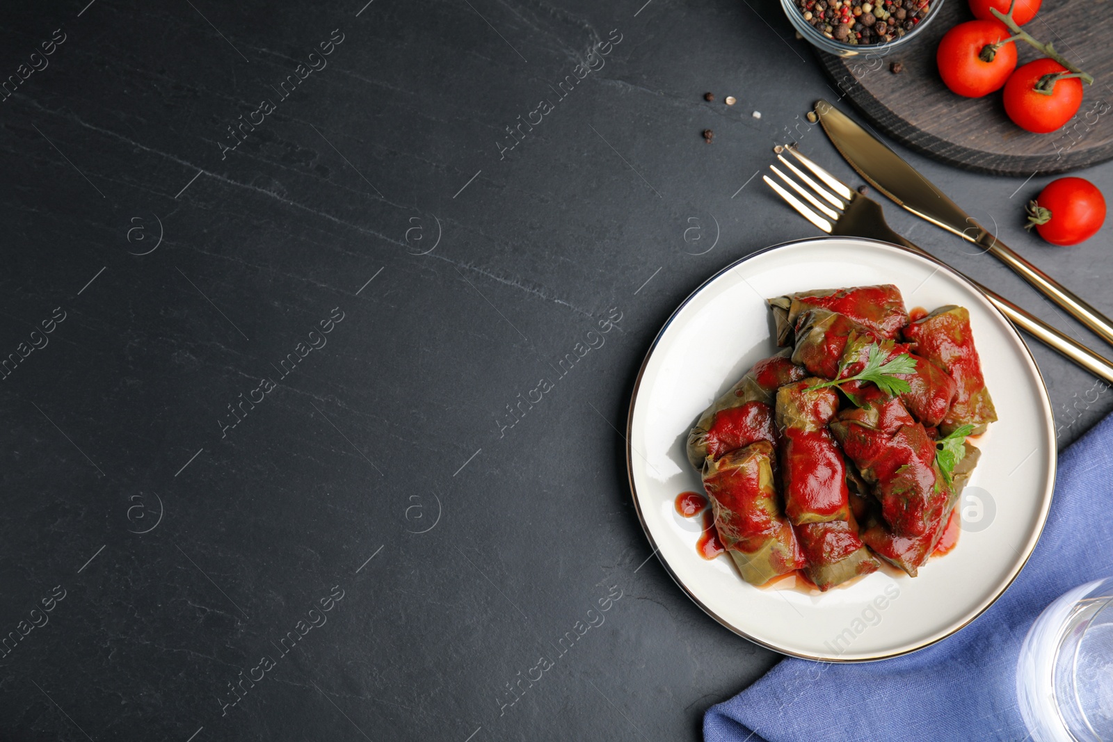 Photo of Delicious stuffed grape leaves with tomato sauce on black table, flat lay. Space for text