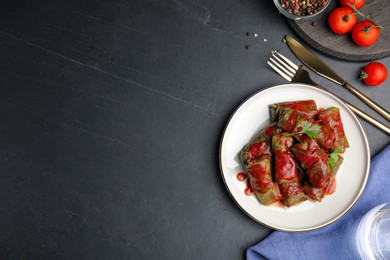 Photo of Delicious stuffed grape leaves with tomato sauce on black table, flat lay. Space for text