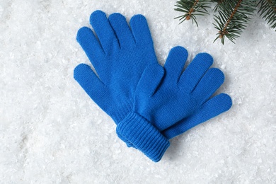 Stylish woolen gloves and fir branches artificial on snow, flat lay