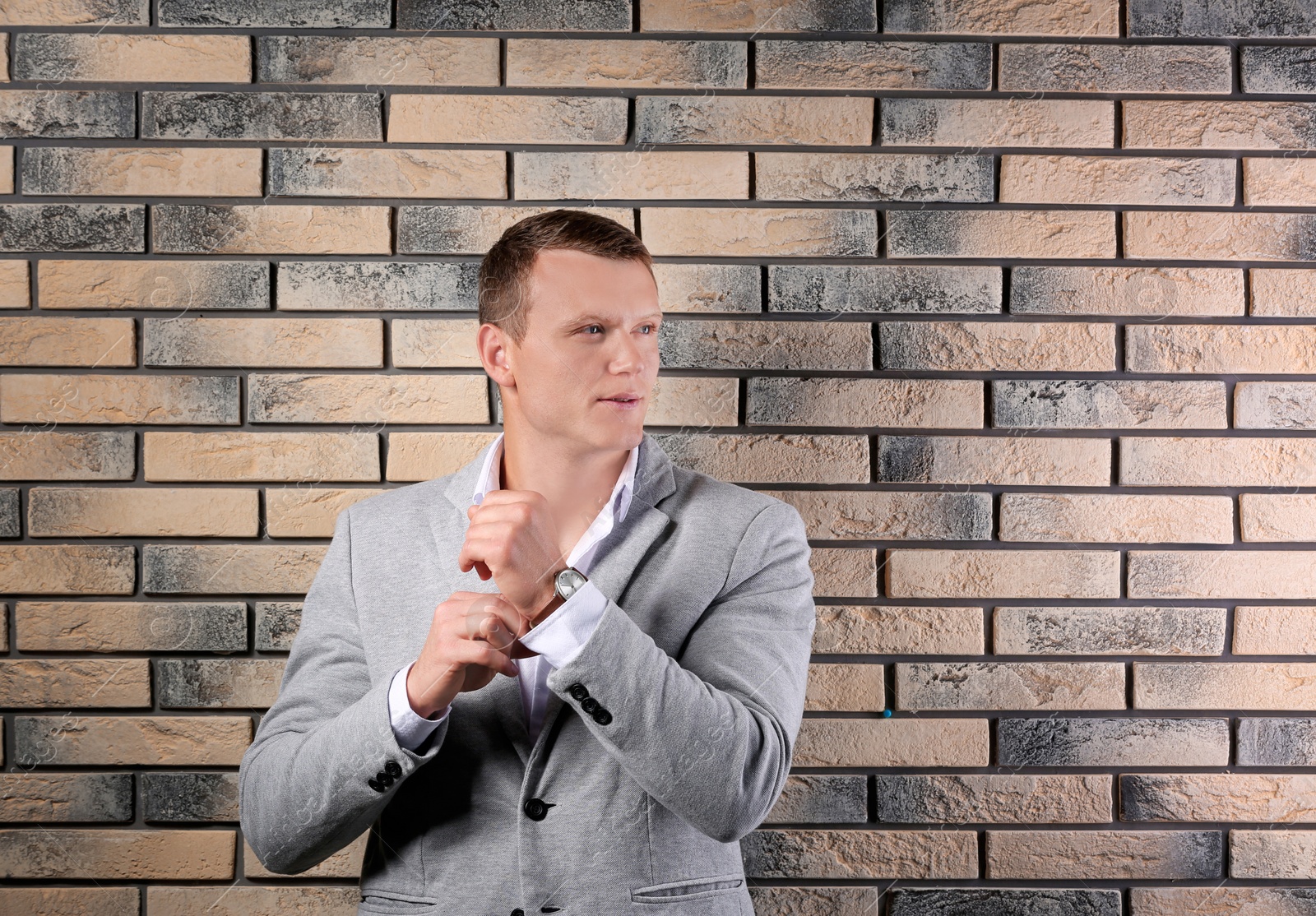 Photo of Handsome young man in suit near brick wall background