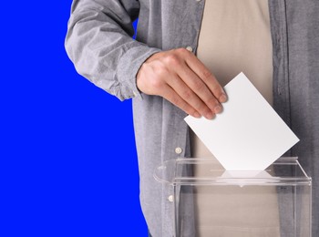 Man putting his vote into ballot box on blue background, closeup