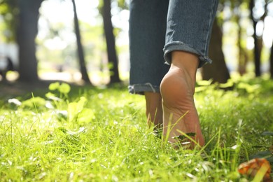 Photo of Woman walking barefoot on green grass in park, closeup. Space for text