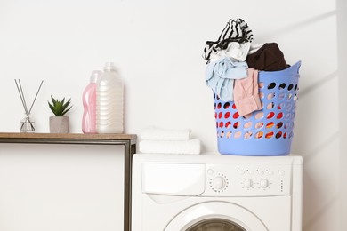 Photo of Laundry basket overfilled with clothes on washing machine in bathroom
