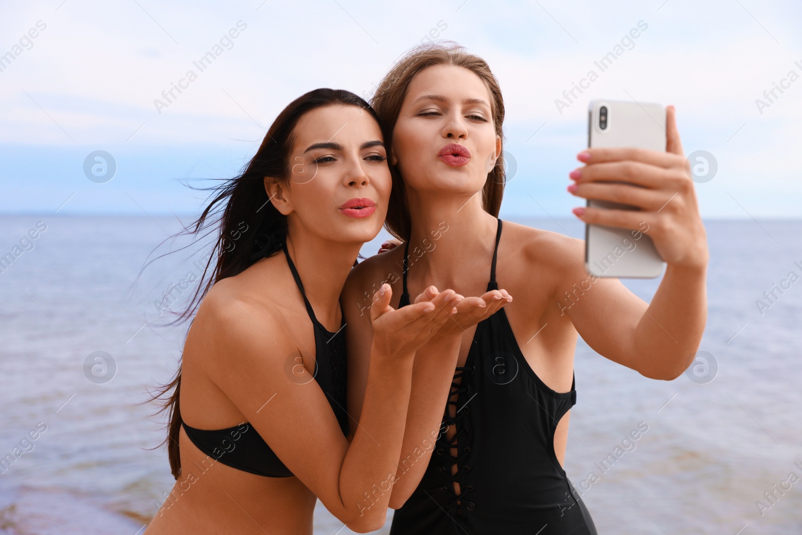 Photo of Young woman in bikini with girlfriend taking selfie on beach. Lovely couple