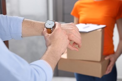 Photo of Closeup view of man checking time near courier with parcels indoors