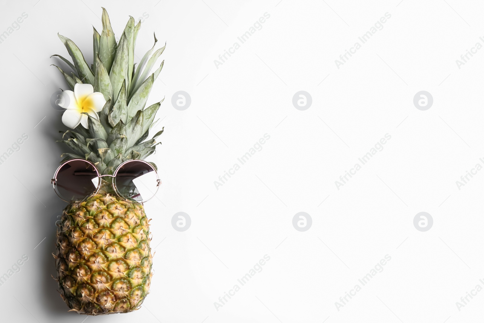 Photo of Pineapple with sunglasses and plumeria flower on white background, top view. Creative concept