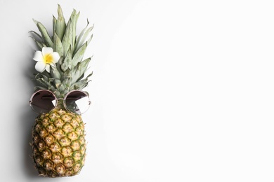 Pineapple with sunglasses and plumeria flower on white background, top view. Creative concept