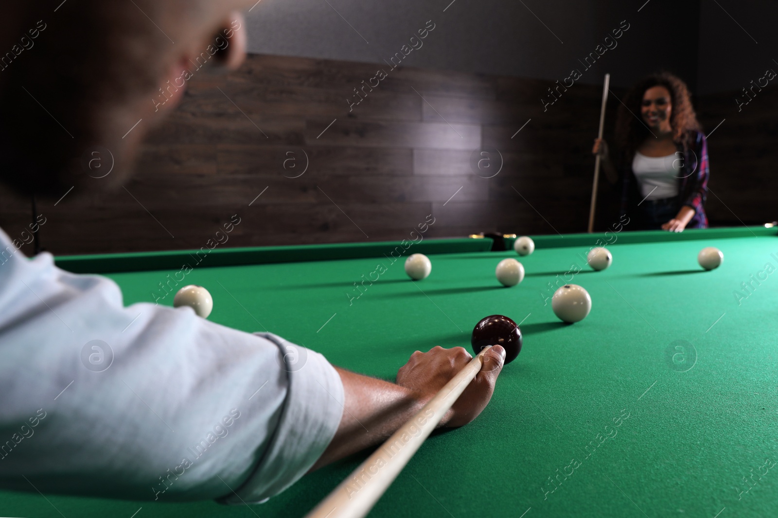 Photo of Young man playing billiard and blurred African-American woman on background, closeup. Space for text