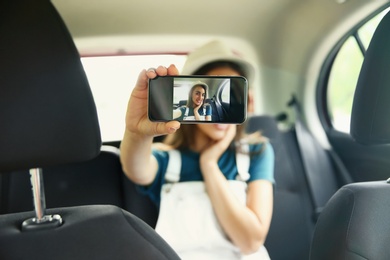 Photo of Happy young woman taking selfie in car