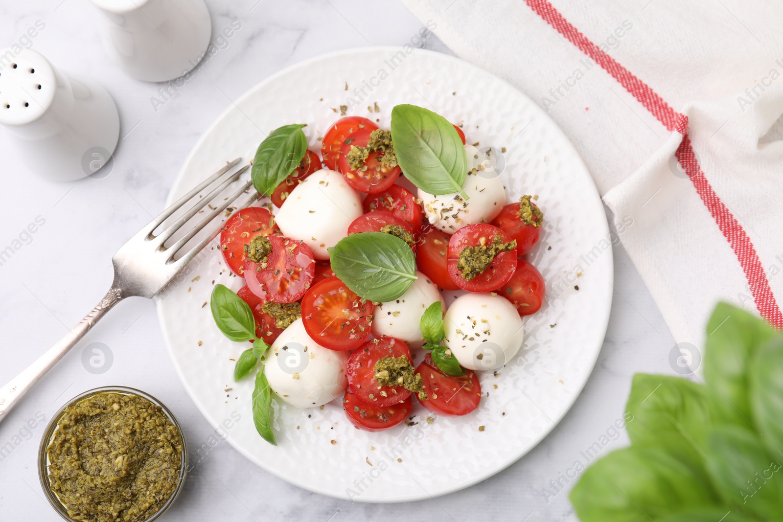 Photo of Tasty salad Caprese with tomatoes, mozzarella balls and basil served on white marble table, flat lay